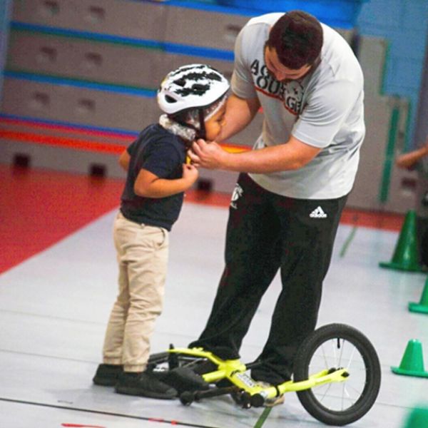 A teacher helps a student put on a bike helmet