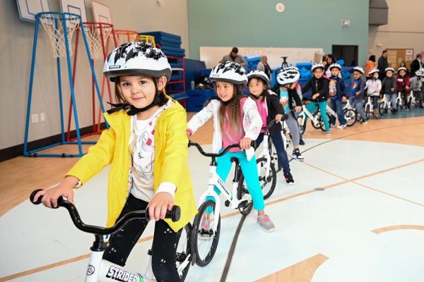 Adults helping children to put on helmets for biking lesson in kindergarten PE gym class