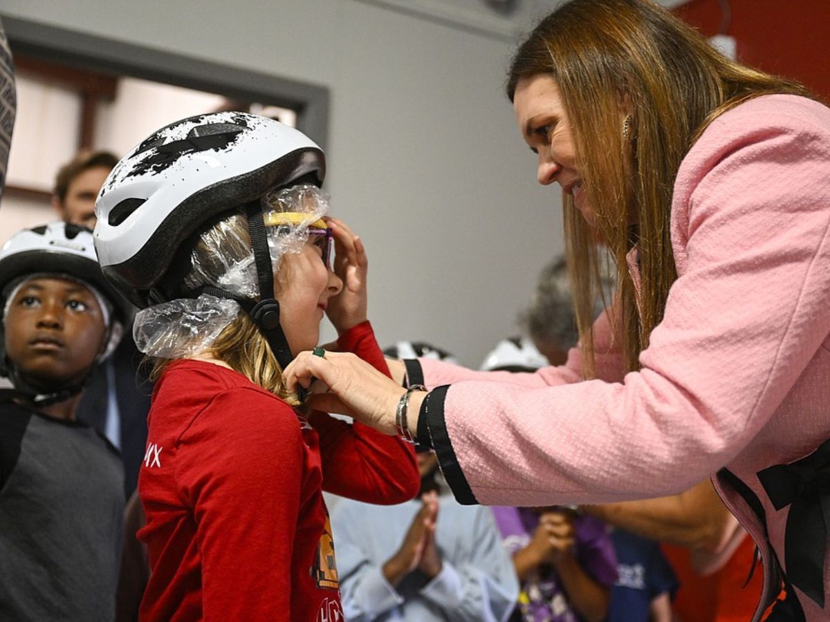 Governor Sanders helps a student put a bike helmet on.