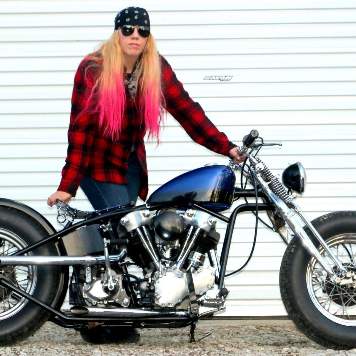 Chris Gibbany poses against a white wall with her blue motorcycle