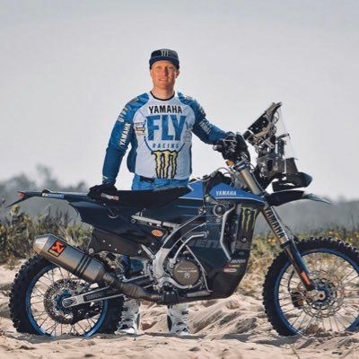All Kids Bike ambassador Andrew Short stands alongside a blue motocross bike in the desert