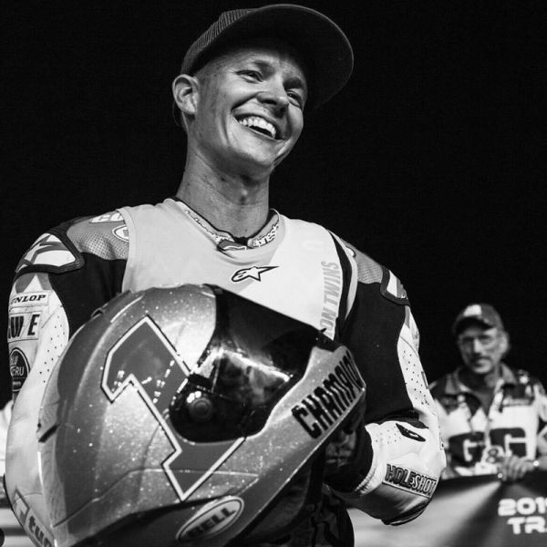 A black and white candid shot of All Kids Bike ambassador Cory Texter smiling and holding his riding helmet after a race