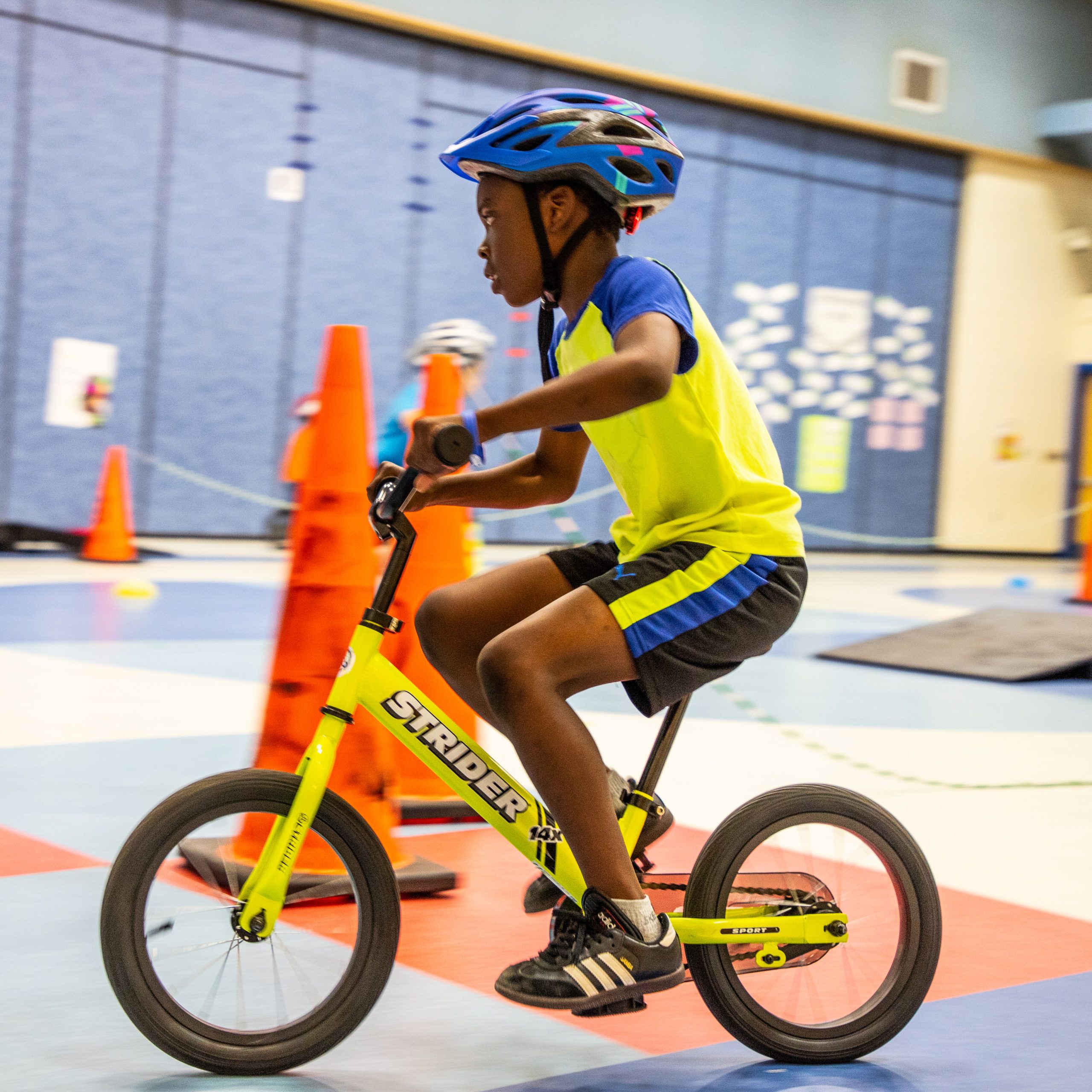 Young boy pedaling green 14x Sport around a cone in PE class