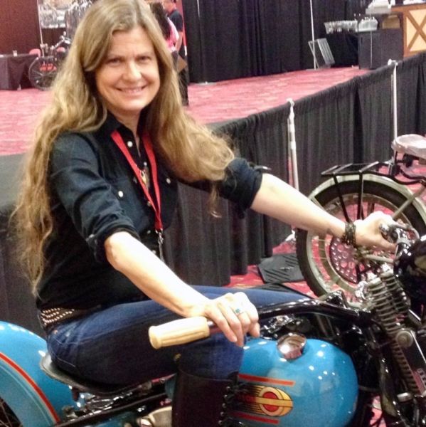 All Kids Bike ambassador Cris Sommer-Simmons sits on a blue vintage motorcycle during a convention