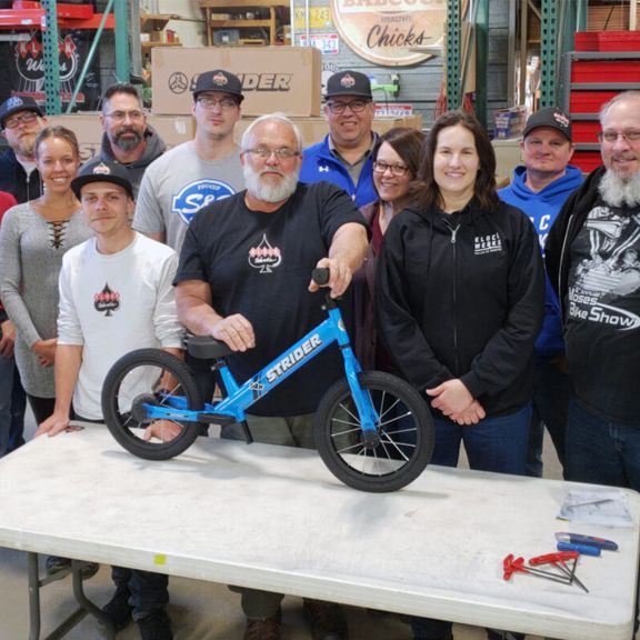 The staff of Klock Werks pose with one of Strider 14x balance bikes they assembled for elementary students in Mitchell, South Dakota