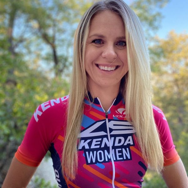 A portrait of All Kids Bike ambassador Nikki Peterson in a pink cycling shirt with trees in the background