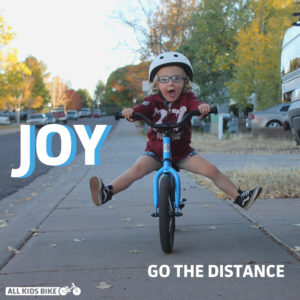 boy riding bike on sidewalk, legs up, smiling 